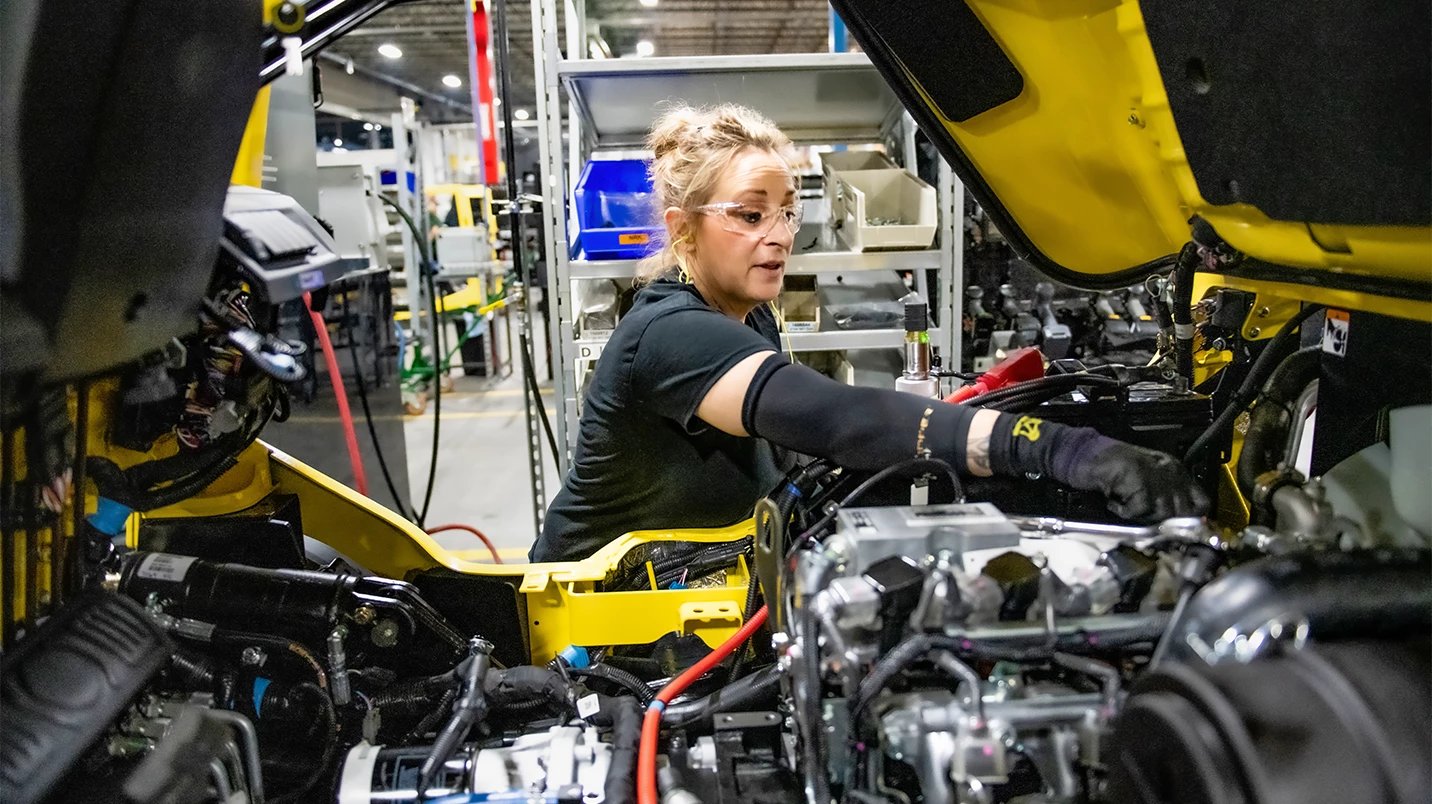 Woman completing final forklift inspection in manufacturing plant.