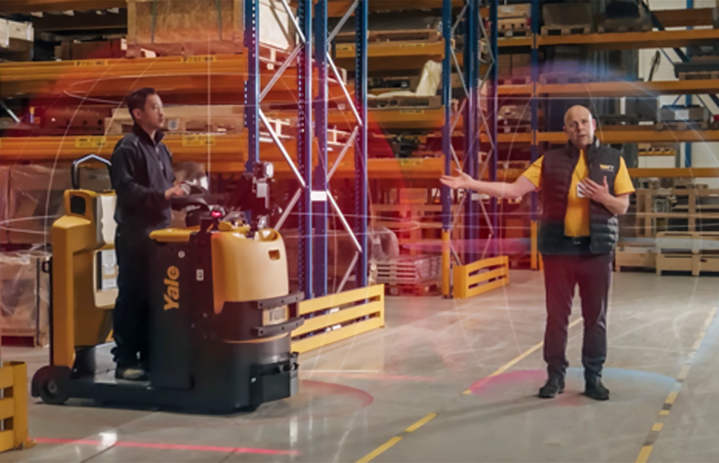An operator driving a Yale tow tractor and another man demonstrate Yale Reliant pedestrian detection in a warehouse.