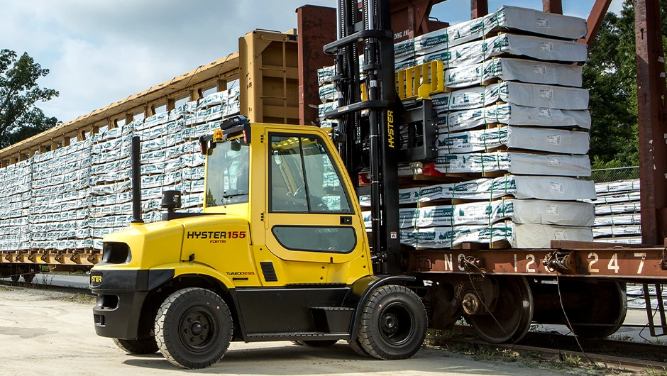 Hyster ICE pneumatic tire forklift lifting heavy load from flatbed trailer. 